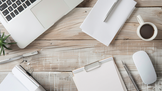 Minimalist office desk with paper pads, notebook, coffee cup, and laptop